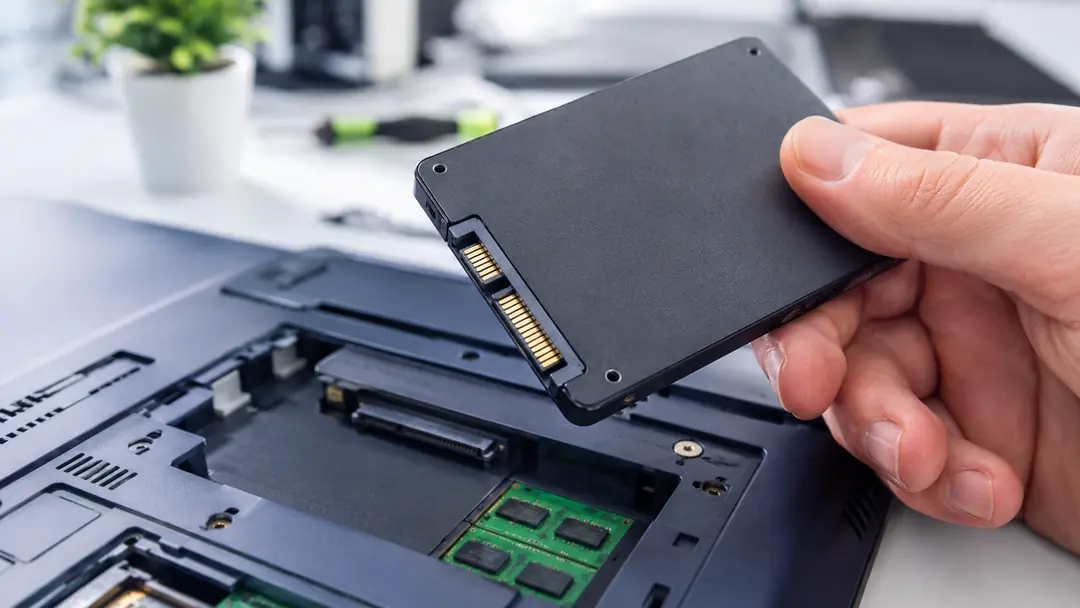 Hand installing a solid-state drive into an open laptop